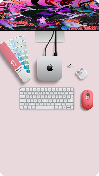 Mac mini, üstten görünüm, gümüş rengi alüminyum, yuvarlatılmış köşeler, ortalanmış parlak siyah Apple logosu, kabloyla bağlı, üstte Studio Display kısmen görünüyor, açık AirPod 4, Pantone renk kartları, sayısal tuş takımlı klavye ve mouse